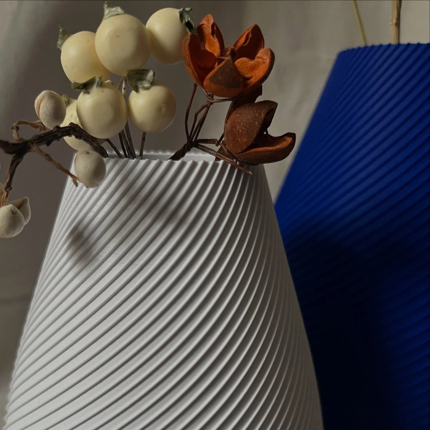White Vertigo vase with pale berries and dried seed pods, cobalt vase behind